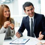 A group of young professionals in a meeting sitting around a white table with papers and a laptop discussing the change management process.