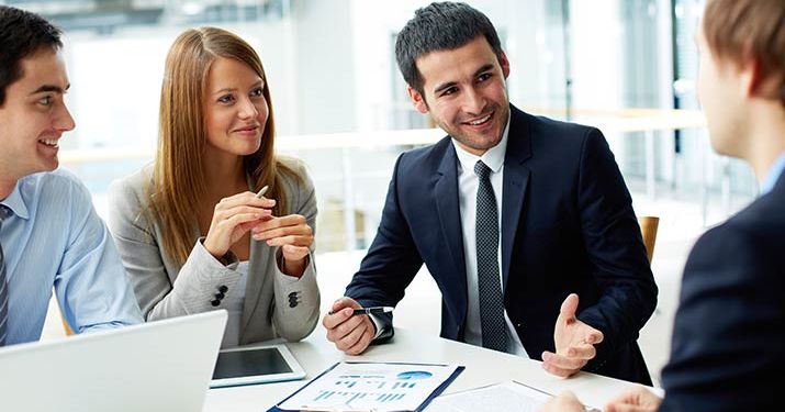 A group of young professionals in a meeting sitting around a white table with papers and a laptop discussing the change management process.