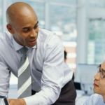 Two men in an office looking at a computer and talking with each other about ecommerce logistics.