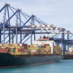 Large cargo ship at a U.S. port with shipping containers being loaded by cranes.