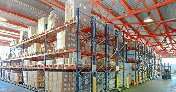 Warehouse in a distribution center filled with boxes and a forklift driving down the aisle.