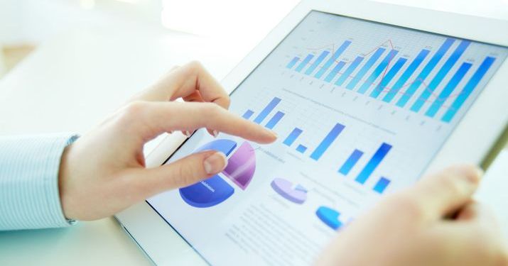 Close up of hands holding a tablet that has bar graphs and pie charts on its screen.