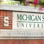MSU brick sign that says in capital green letters "Michigan State University" and below that in smaller letters on a concrete slab it says "The Pioneer Land Grant College".