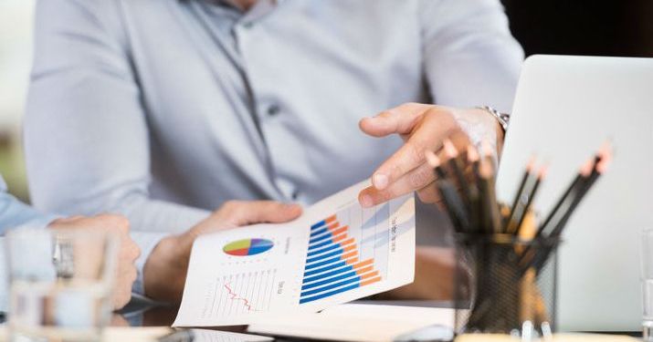 Close up shot of sitting at a desk holding a piece of paper with bar charts on it.