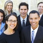 Nine employees from all over the world dressed in business attire standing together for a group photo.