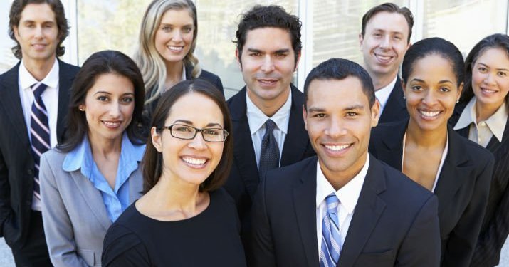 Nine employees from all over the world dressed in business attire standing together for a group photo.