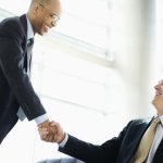 Two business men in a lobby shaking hands after a successful negotiation.