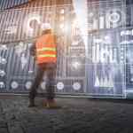 Man in an orange reflective vest and hard hat looking at metal shipping containers that have supply chain graphics and data holographically displayed on them.