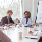 Mature female doctor gestures while discussing something during a healthcare conference with colleagues.