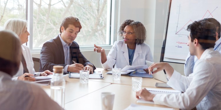 Mature female doctor gestures while discussing something during a healthcare conference with colleagues.