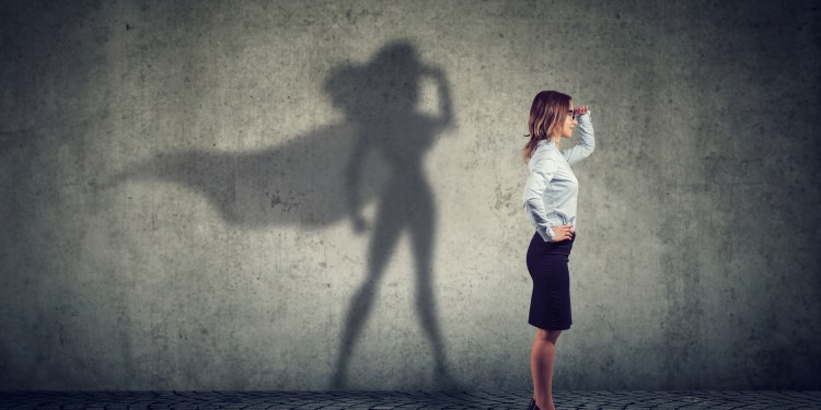 Side view of a business woman with her shadow resembling a super hero with cape, looking aspired.