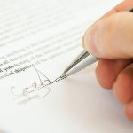A pen signing the signature line on a contract.