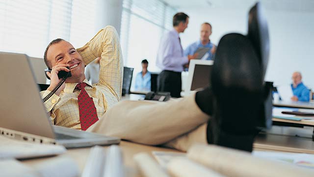 A man talking on the phone, sitting with his feet propped up on his desk.