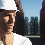 A man in a shipping yard wearing a white construction hat.