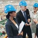 A group of managers in a warehouse wearing blue constructions hard hats.