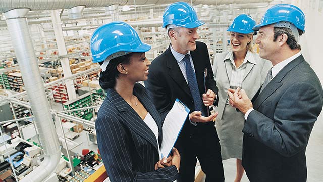 A group of managers in a warehouse wearing blue constructions hard hats.