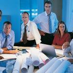 A group of employees looking at a table with a pile of rolled up blueprint papers.