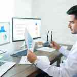 Business analyst analyzing business performance data while holding paper at desk