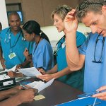 A group of medical professionals working together on paperwork wearing scrubs and stethoscopes.