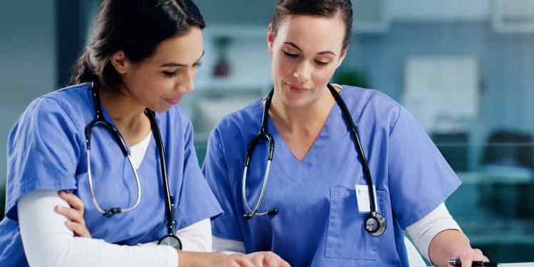 bpm in healthcare depicted by two nurses discussing business process management with a clipboard and tablet device in a healthcare facility