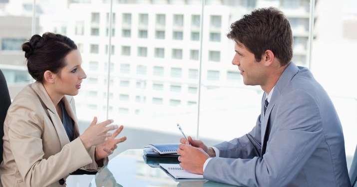 A businessman and a businesswoman sitting down across a table talking to each other.