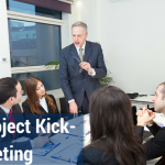 Employees in a conference room listening to a man standing up and talking.