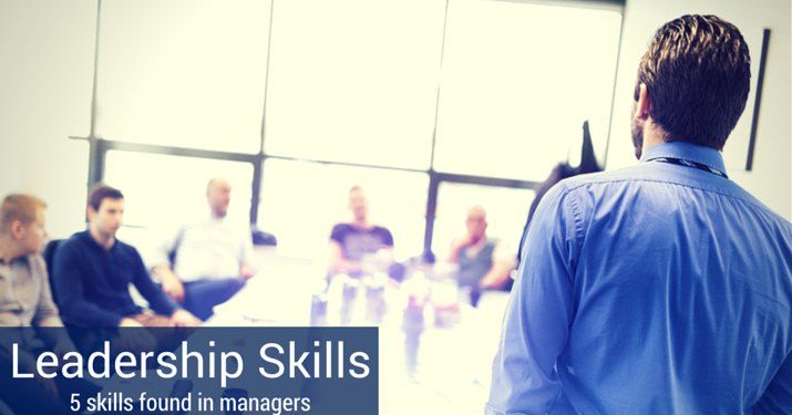 Leadership skills for managers depicted by co-workers sitting around a conference room table, listening to a man who is standing up and speaking about leadership skills managers should have.