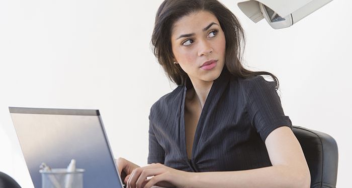 A woman on her computer looking over her shoulder under the watchful eye of a large security camera right next to her.