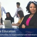 A sign that says "Corporate Education" with a business woman behind it smiling and five more co-workers in the background on a computer and talking to each other.