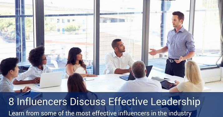 A bunch of people sitting around a boardroom table listening to a man at the head of the table giving a presentation in front of a large window.