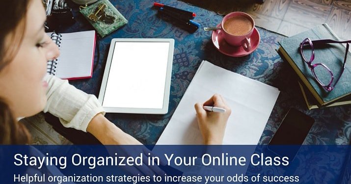 A woman writing on a piece of paper studying for her online classes with a tablet, coffee, notebook, glasses, and phone on a blue table.