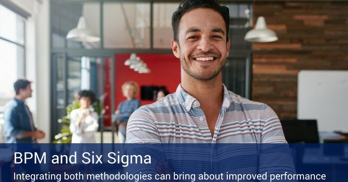 A man smiling into the camera with other employees in the background of the office and a banner across the bottom of the picture that reads "BPM and Six Sigma".