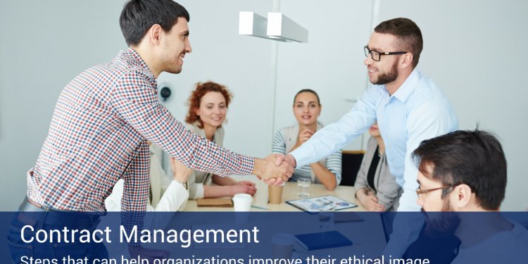 Two men greeting each other in an office shaking hands while two other co-workers are sitting down at a table behind them.