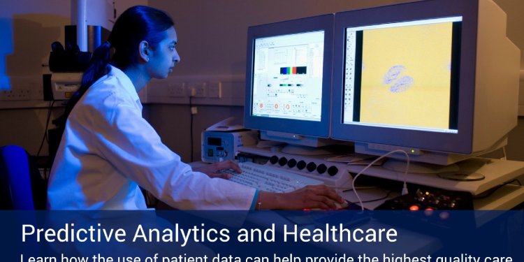 Healthcare employee in a white lab coat looking at two big computer screens with data and microscopic images with medical equipment behind her.