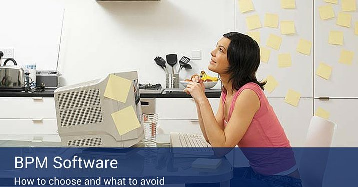 A woman looking up and thinking in her office with post-it notes all over her computer and the wall beside her.