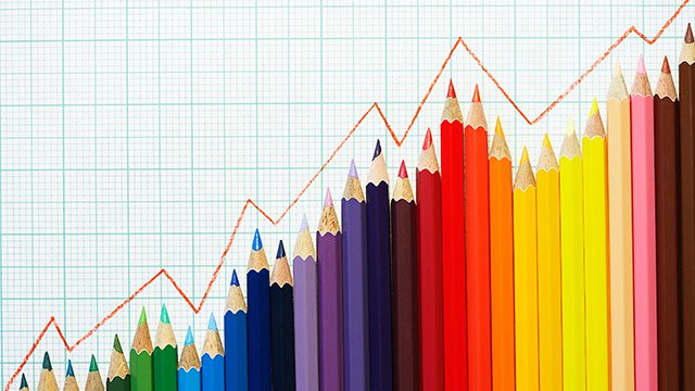 Illustrated line graph following a trend line on top of a row of colored pencils against graph paper.