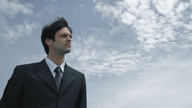 A businessman outside looking up on a sunny day with a beautiful blue sky.