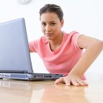 A woman sitting at her computer with her hands on the desk stretching.