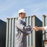 Two men shaking hands outside in a shipping yard.