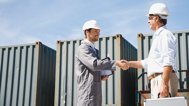 Two men shaking hands outside in a shipping yard.