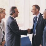 Four people coming together for a business meeting while two of them shake hands.
