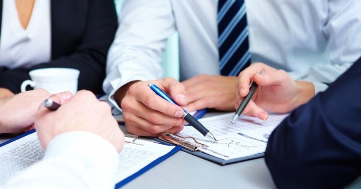 Hands of a business professional writing with a pen on a contract on a clipboard.