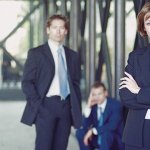 Three business people posing for a picture, with a woman standing in front with her arms crossed and two men standing behind her.