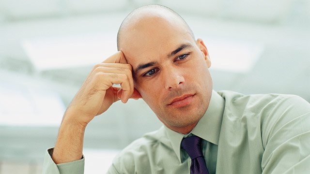 A man wearing a dress shirt and tie with his hand on his head looking down thinking.