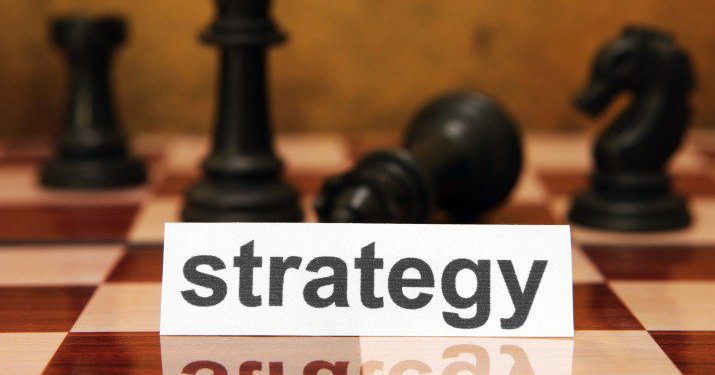 A chessboard with chess pieces scattered across the board and a white piece of paper on it that says strategy.