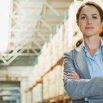 A woman in a warehouse with her arms crossed smiling into a camera.