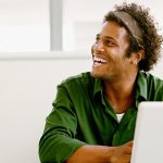 A man looking up smiling and laughing while workingn on information security on his computer.