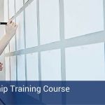 White pieces of paper hung up on a wall with a woman writing on them, preparing to start a leadership training course.