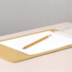 A white table with a wooden clipboard and a blank white sheet of paper and a yellow wooden pencil.