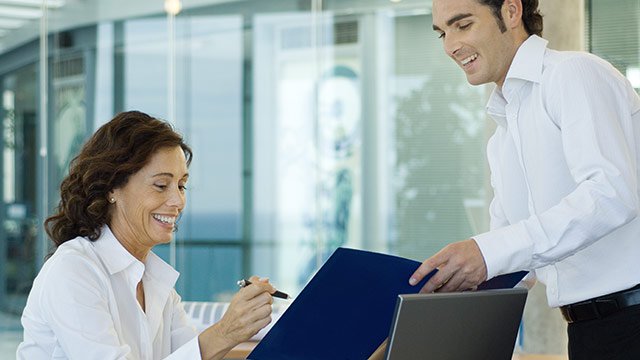 A man and a woman looking at a blue folder that the man is holding for her to sign papers in the folder.